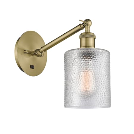 A large image of the Innovations Lighting 317-1W-13-5 Cobbleskill Sconce Antique Brass / Clear