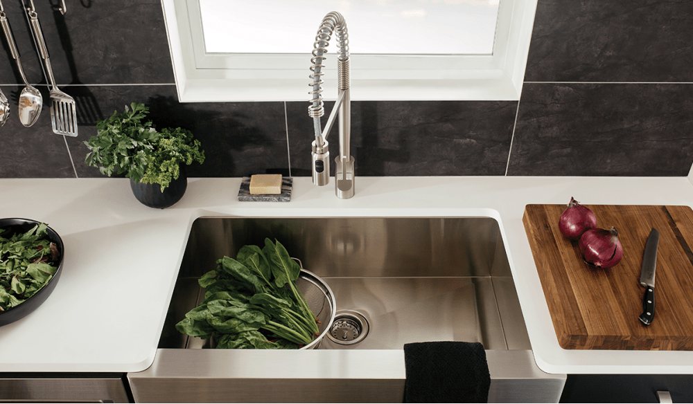 Stainless steel kitchen sink, spinach, red onions on meat board.