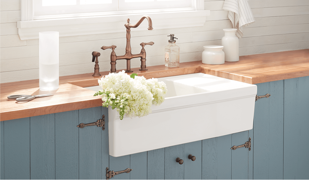 White farmhouse sink, flower bouquet, copper bridge faucet.