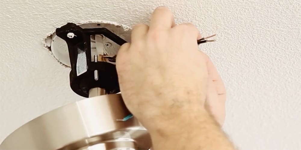 Hands holding wires from ceiling and fan.