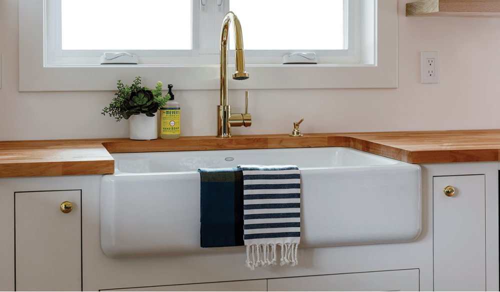 White cast iron farmhouse style sink, gold faucet.