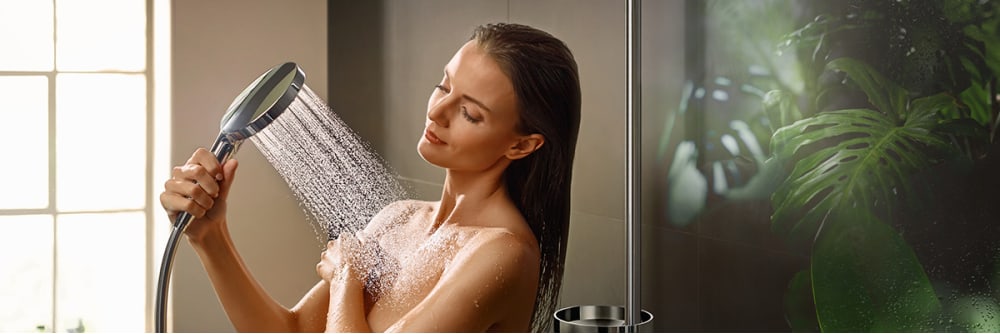 Woman holding Radiance Hand Shower in chrome, plants in background.