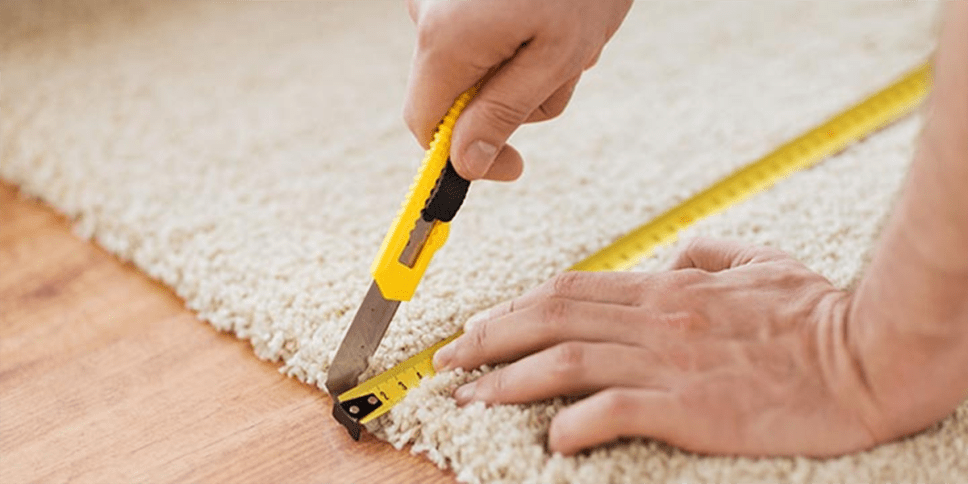 Hand on white carpet, yellow measuring tape, yellow cutting blade.