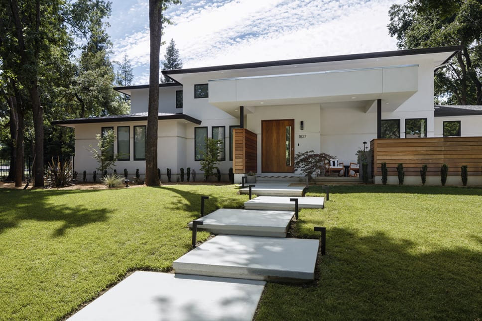 Modern white house, green grass in yard, cement stepping stones, trees.