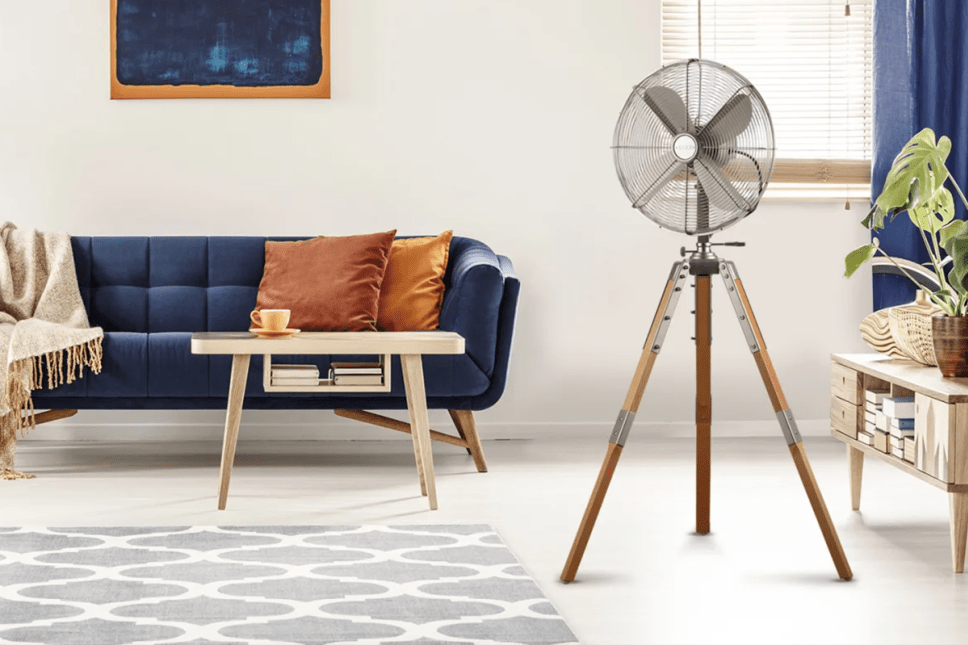 Floor standing fan with 3 wooden legs in modern living room with blue sofa.