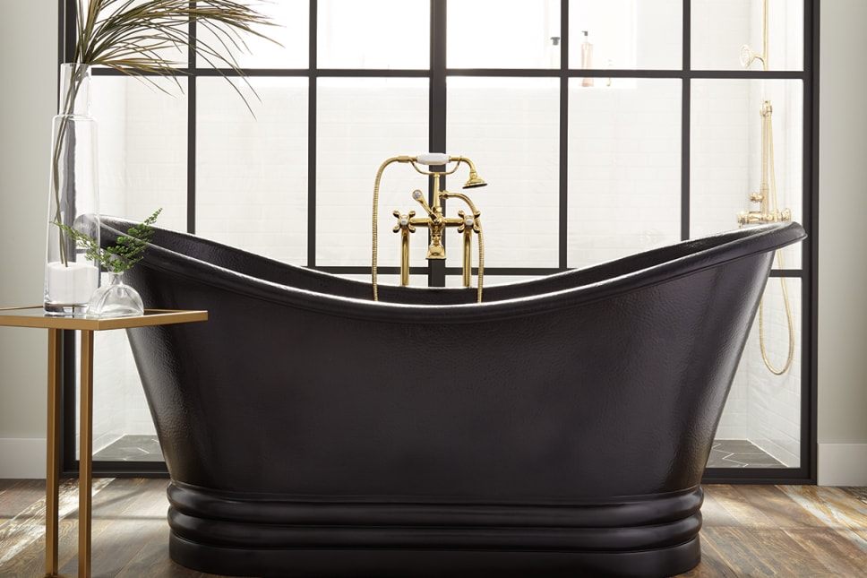 black slipper shape tub with gold faucet. Palm leaf, glas vase, white sand