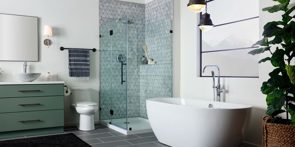 Oval tub, gray geometric tile, soft green cabinets, dark gray tile floor.