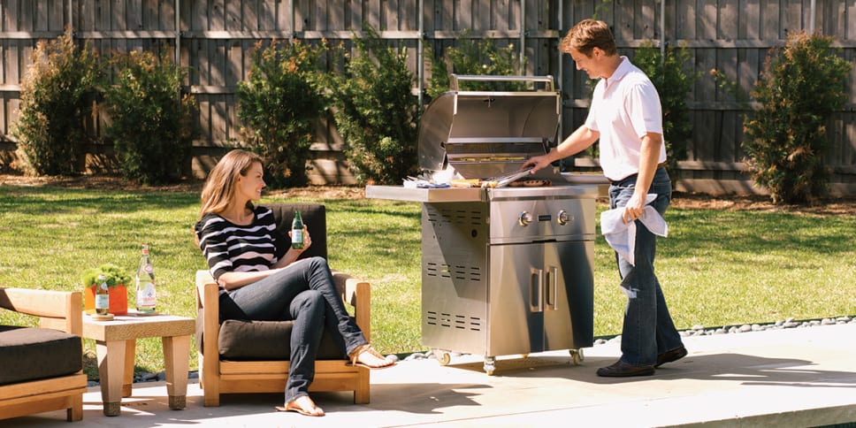 Coyote freestanding grill. Man and woman drinking and cooking, grass.