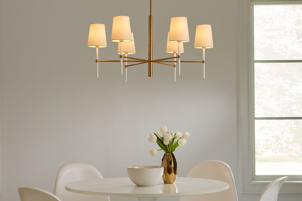 6 light chandelier with brass and white finish over modern dining table.